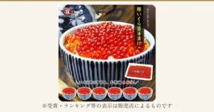 白いご飯にのせた鱒いくら醤油漬けの丼（染付の茶碗）と、トレーに入った越前かに職人甲羅組の商品、手前に小さな丼6杯を並べた商品写真。画像内に店舗ロゴ「越前かに職人 甲羅組 DENSHOKU」、縦書きの「鱒いくら醤油漬け」、店舗が画像に入れた表示「一級品の原卵を国内加工」「特盛500g」「いくら丼にすると、お茶碗6杯分！」あり。下に「※受賞・ランキング等の表示は販売店によるものです」