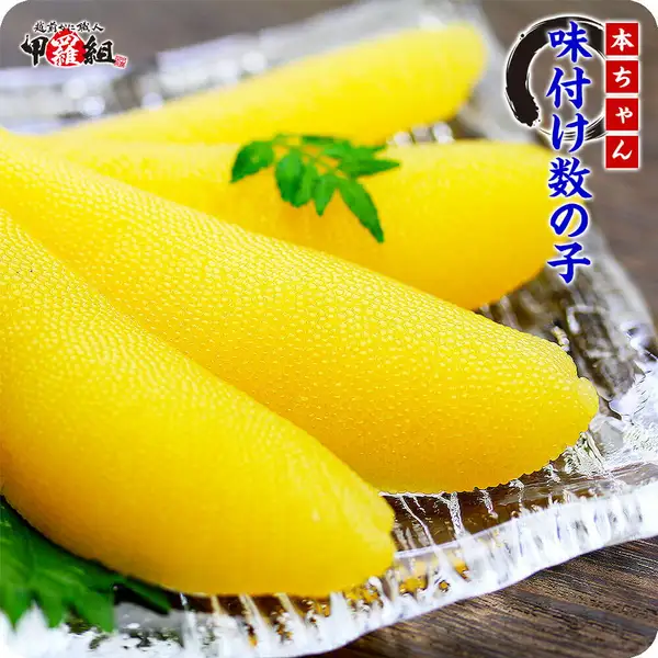 越前かに職人甲羅組の味付け数の子(にしん卵)3本を透明な器の上に大葉などの葉とともに盛り付けた写真。画像内に店舗ロゴ「越前かに職人 甲羅組」、朱色の枠で「本ちゃん」、紺色の文字で「味付け数の子」の表示あり