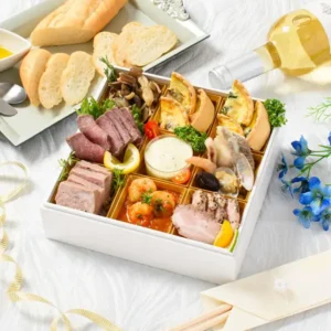 白い正方形の重箱に彩りよく盛り付けたふらんす屋 洋風おせち『ヌイイ』料理セットの写真。ローストビーフ、パテ、キッシュ2種、海老とトマトのマリネ、貝と海老の盛り合わせなどが並び、手前にバゲットとオリーブオイル、奥に白ワインのボトルが添えられている（重箱・食器・パン・ワインは商品に含まれません）