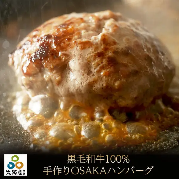 Product photo of the 100% Kuroge Wagyu handmade hamburg steak, a close-up of it being seared on a hot iron plate with juices bubbling and steam rising. Text the shop placed in the image reads: a round “Osaka-made” (大阪産) logo and “黒毛和牛100% 手作りOSAKAハンバーグ” (100% Kuroge Wagyu Handmade OSAKA Hamburg).