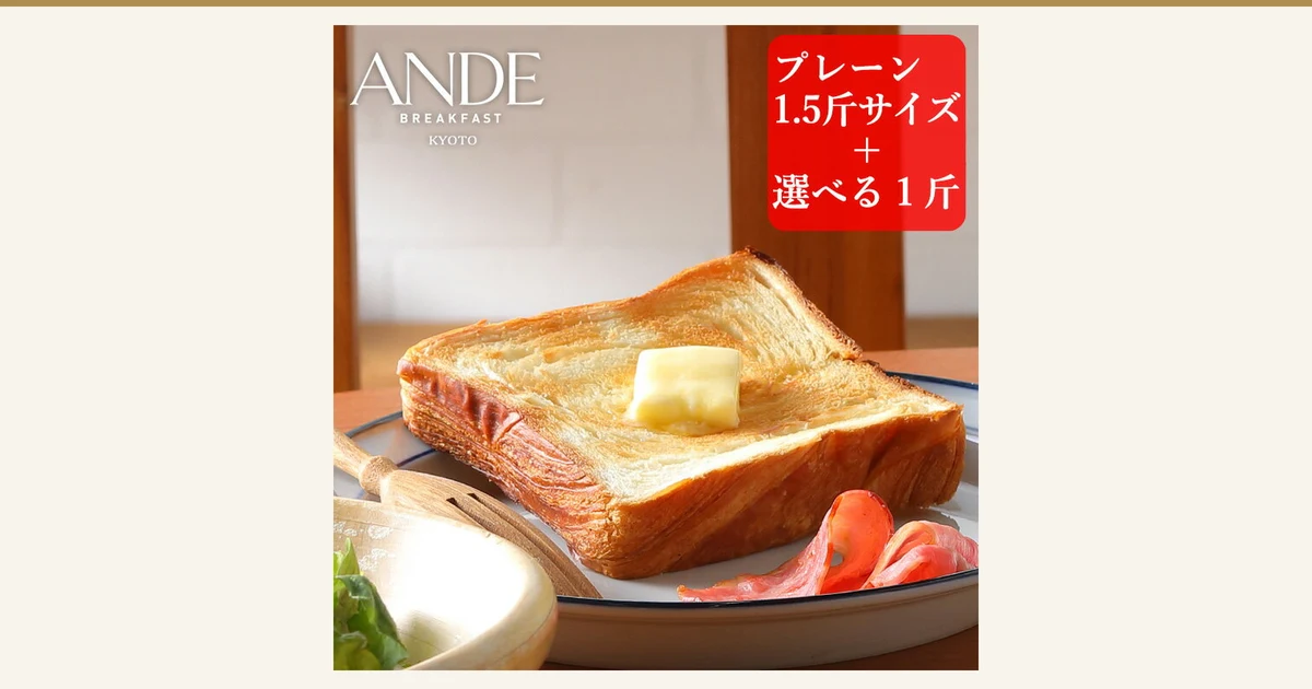 Product photo of a slice of Danish bread toasted with a pat of butter on top, on a white plate, with ham at the edge of the plate and lettuce in a wooden bowl in front (ANDE Danish Bread, plain 1.5-kin loaf + 1-kin loaf of your choice). Text the shop placed in the image: “ANDE BREAKFAST KYOTO”, “プレーン1.5斤サイズ＋選べる1斤” (plain 1.5-kin size + 1-kin loaf of your choice)