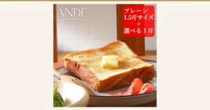 バターをのせて焼いたデニッシュ食パン1枚が白い皿に置かれた商品写真。皿の端にはハム、手前の木の器にはサラダ菜も写っている（アンデ デニッシュ食パン プレーン1.5斤＋選べる1斤）。店舗が画像に入れた表示「ANDE BREAKFAST KYOTO」「プレーン1.5斤サイズ＋選べる1斤」