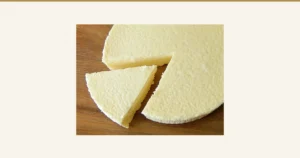 木の板の上に置いた濃厚チーズケーキから、三角に1切れを切り分けた写真（フロム蔵王 大感動！濃厚チーズケーキ2個セット）。表面と断面は薄い黄色です