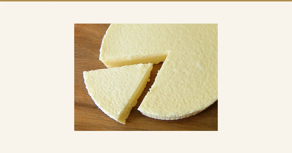 木の板の上に置いた濃厚チーズケーキから、三角に1切れを切り分けた写真（フロム蔵王 大感動！濃厚チーズケーキ2個セット）。表面と断面は薄い黄色です