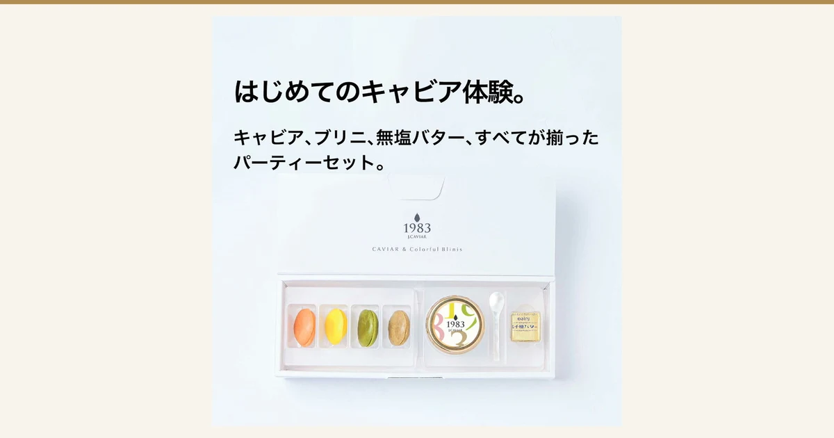 Product photo of the Miyazaki Caviar 1983 (12g) & Blini Set: inside a white gift box lie four blini in orange, yellow, green and brown, a caviar jar with a white, gold-rimmed lid printed with “1983”, a shell spoon and a gold-wrapped butter. Text the shop placed in the image reads “はじめてのキャビア体験。” (Your first caviar experience.) and “キャビア、ブリニ、無塩バター、すべてが揃ったパーティーセット。” (A party set with caviar, blini and unsalted butter, all included). The box and lid are printed with “1983 J.CAVIAR” and “CAVIAR & Colorful Blinis”.