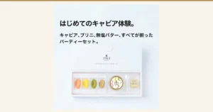 白い化粧箱の中に、オレンジ・黄・緑・茶の4色のブリニ4枚、「1983」の文字が入った白いふた(金の縁)のキャビアの瓶、貝のスプーン、金色の包みのバターが並んだ宮崎キャビア 1983 (12g) & ブリニ セットの商品写真。店舗が画像に入れた表示として「はじめてのキャビア体験。」「キャビア、ブリニ、無塩バター、すべてが揃ったパーティーセット。」の文字。箱とふたには「1983 J.CAVIAR」「CAVIAR & Colorful Blinis」の印字。