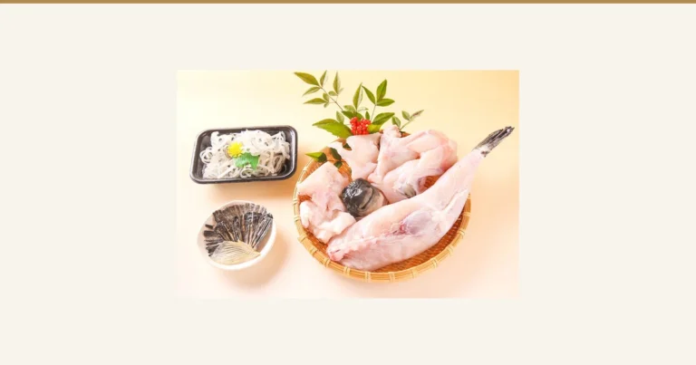 Product photo of bone-in torafugu migaki meat and a whole body on a bamboo basket, decorated with nandina leaves, with a black tray of sliced tessa skin and a small dish of fins beside it, for the 淡路島3年とらふぐ 若男水産 whole-fish migaki