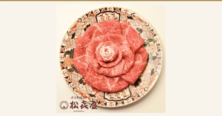 将近江牛寿喜烧用的切片肉（里脊肉・后腿肉・牛腩）摆成玫瑰花形、盛在红橙黑花纹圆盘上的商品照片。图片内有店铺标志及文字“近江松喜屋牛”“松喜屋 MATSUKIYA”（店铺自行加入的标示）。近江牛 松喜屋 すき焼き 特選 1kg