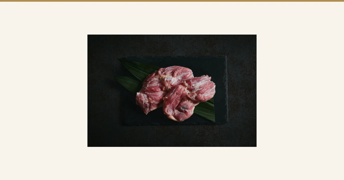Product photo of Purebred Nagoya Cochin Chicken Thigh 1kg, Morning-Slaughtered: raw chicken thighs arranged on black slate lined with bamboo leaves. No text appears in the image.