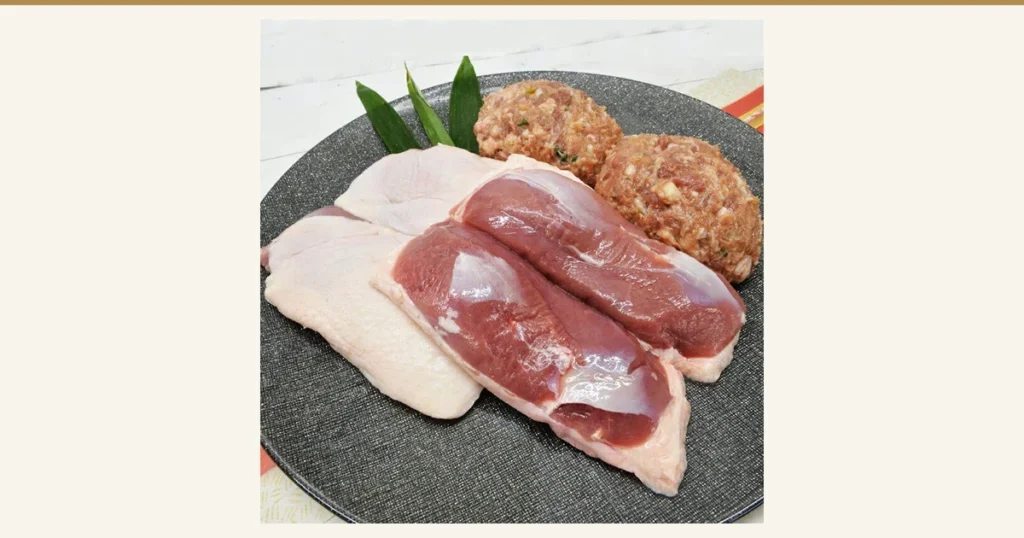 Product photo of the 鴨鍋三昧セット (Duck Hot Pot Set): skin-on duck meat and two duck meatballs on a gray round plate with leaves