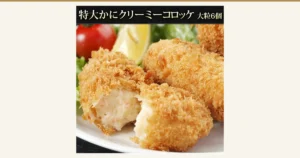 魚耕 カニクリームコロッケ 大粒6個のアイキャッチ。皿に盛った揚げコロッケと、割った断面から白いクリームが見える商品写真。レモン・ミニトマト・レタスは盛り付け例で、商品には含まれない。画像内に店舗が画像に入れた表示として「特大かにクリーミーコロッケ 大粒6個」の文字あり。