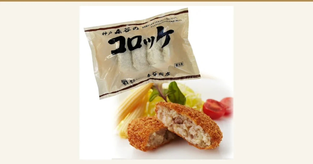 神戸森谷のコロッケ 10個（本神戸肉森谷商店）の商品写真。「神戸 森谷の」「コロッケ」「森谷商店」「要冷凍」「お肉屋さんが作ったなつかしい味のコロッケ。」「すじ入りでコリコリッとした食感が楽しい。」と印字された袋に入った揚げる前の白い衣のコロッケと、手前に割って断面を見せた揚げたコロッケ2個、ヤングコーン・葉物野菜・ミニトマト。野菜は盛り付け例で、商品に含まれません。