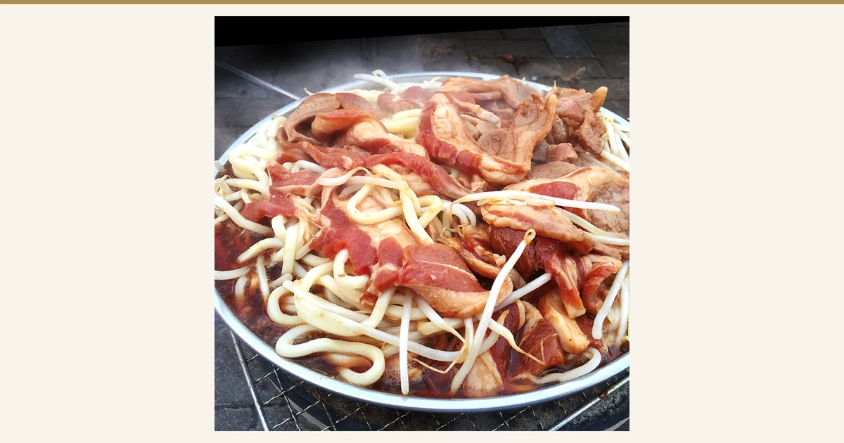 丸い鉄板の上にラム肉ともやし、うどんをのせて焼いている調理例の写真(味付きジンギスカン ラム肉 厚切 1kg)。もやし・うどんは商品に含まれません