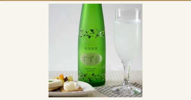 Product photo of Ichinokura Sparkling Sake Suzune 300ml in a green bottle decorated with a pattern of leaves and red berries. The bottle label shows the text “いちのくら”, “発泡清酒”, “すず音”, “Sparkling Sake SUZUNE”, and “お酒”. On the right is a tall, slender glass of cloudy white sake, and at the bottom left is a plate of crackers topped with cheese and fruit.