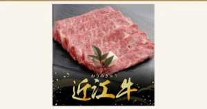黒い石板の上に霜降りの牛肩ロースの薄切り肉を重ねて並べ、飾りの葉と白い飾りが添えられた商品写真（千成亭 近江牛 肩ロース スライス すき焼き用 500g）。店舗が画像に入れた表示として「おうみぎゅう」「近江牛」の文字