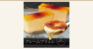 Product photo of Crème Brûlée Catalana, 2 Pieces (クレームブリュレ 2本入 カタラーナ): two long bars with a burnt-caramel top on a gray slate, and a spoon in front holding a piece with creamy custard dripping from it. Text the shop placed in the image: “焦がしカラメル クレームブリュレ 2本入” (burnt caramel crème brûlée, 2 pieces) and “Burnt caramel Creme brulee”