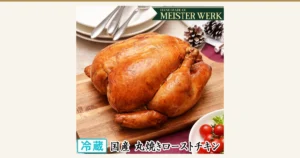 木のまな板にのせた国産若鶏の丸焼きローストチキン1羽の商品写真（近江牛の千成亭）。皿・ナイフとフォーク・松ぼっくり・トマトなどの盛り付けは盛り付け例で、商品には付属しません。店舗が画像に入れた表示「HAND MADE OF MEISTER WERK」「冷蔵」「国産 丸焼きローストチキン」