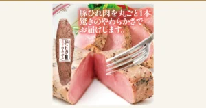 豚ひれ肉のローストポークの商品写真。ラベルの付いた1本と、フォークで切り分けたピンク色の断面。店舗が画像に入れた表示「豚ひれ肉を丸ごと1本 驚きのやわらかさでお届けします。」「豚ひれ肉のやわらかローストポーク」「米久」（米久 豚ひれ肉のローストポーク 約360g）
