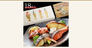鳥取門永 西京漬＆粕漬ギフトセット「雅」6種18点の商品写真。焼き上げた銀だら・紅鮭・さわらの切り身とイカが皿に盛られ、レモン、すだち、しそ、みょうが、大根おろしなどが添えられている。右上に金色の魚の絵柄の外箱と、個包装された切り身が写っている。店舗が画像に入れた表示として「18点入」の文字あり。