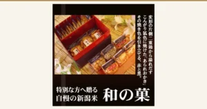 赤い内張りの黒い重箱型のギフト箱と、箱の中と手前に並ぶ個包装のあられおかきの商品写真。店舗が画像に入れた表示として「変形の片側二重箱から溢れだす」「こんがり狐色に焼けた『あられおかき』」「その焼き色を引き立てる、赤と黒。」「特別な方へ贈る」「自慢の新潟米」「和の菓」と書かれている。加藤製菓 おつまみ重箱ギフト G50（17袋入り）