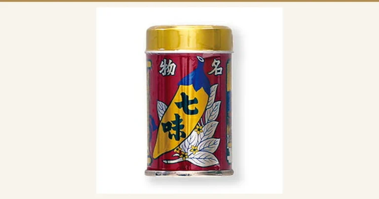 七味辣椒粉罐装商品照片：红色罐身印有「名物 七味」字样，带金色罐盖（八幡屋礒五郎 七味缶 14g）。