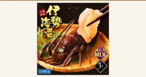殻付きの伊勢海老（千葉県産 天然 3尾 1.2kg 特大・大MIX）の商品写真。竹ざるに殻付きの伊勢海老1尾をのせ、箸でつまんだ半透明の薄い身が添えられている。店舗が画像に入れた表示「千葉県産」「伊勢海老」「特大・大MIX」「3尾入」「冷凍配送」