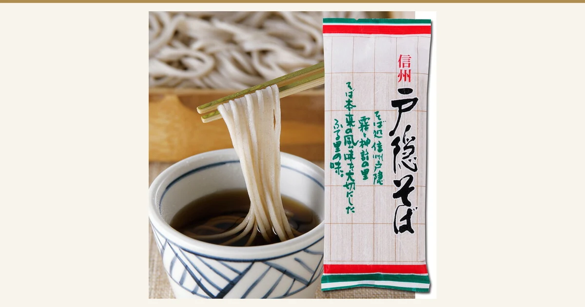 Product photo showing, on the left, soba lifted with chopsticks and dipped into brown tsuyu dipping sauce in a white bowl with an indigo pattern, and on the right a tall bag of Shinshu Togakushi Soba (white with green ruled lines and red and green bands at top and bottom); soba on a wooden tray is visible behind. The bag is printed with “信州”, “戸隠そば” and “そば処信州戸隠 霧と神話の里 そば本来の風味を大切にしたふる里の味。” (printing on the bag). The tsuyu is a serving suggestion and is not listed in the set contents on the product page. 信州戸隠そば お試しセット