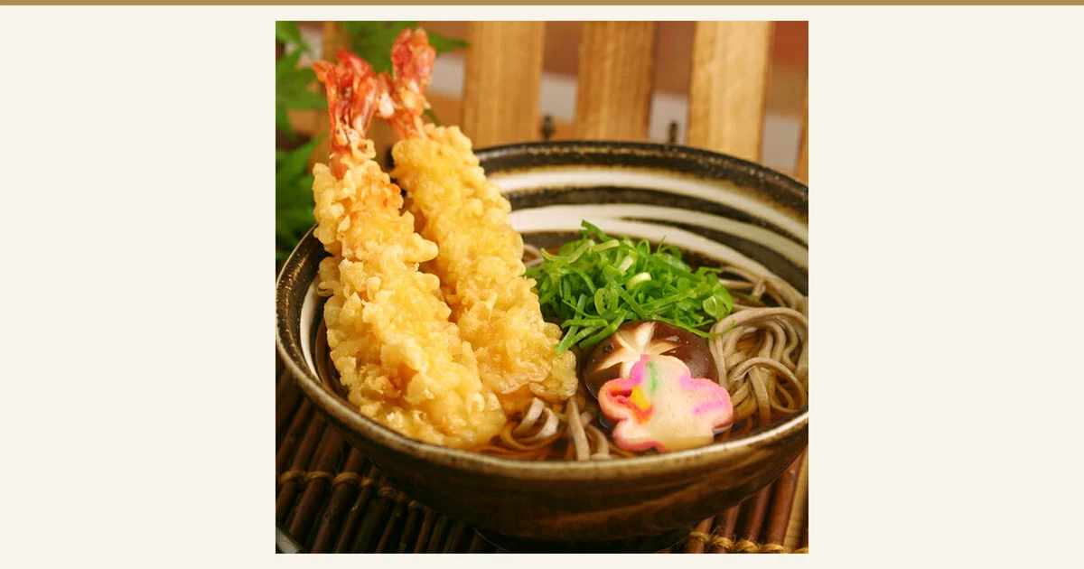 茶色の器に盛った温かいそばに、えび天2本・刻みねぎ・しいたけ・花形のかまぼこをのせた写真(本田商店 出雲だんだんそば 6人前)