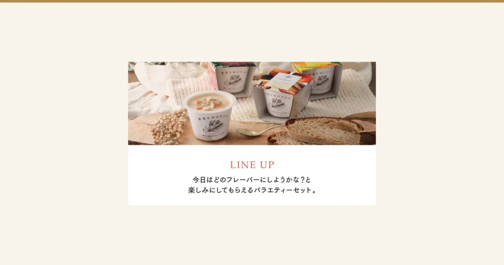 木の台の上に、ふたを開けたクラムチャウダーのカップ（にんじんやじゃがいもなどの具が見える）と、紙のスリーブに入った白いカップ3つ、金色のスプーン、切ったパン、白い実の枝を並べた商品写真（野菜をMOTTO 国産野菜スープ おまかせ6個ギフトセット）。カップに「野菜をMOTTO」「More vegetables in life」の印字、中央のスリーブに「Clam chowder」「あさりと国産野菜の濃厚クリーミーなクラムチャウダー」「Made in Japan」の印字。店舗が画像に入れた表示として「LINE UP」「今日はどのフレーバーにしようかな？と楽しみにしてもらえるバラエティーセット。」の文字