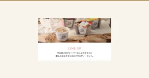木板上摆放着一杯打开盖子的蛤蜊浓汤（可见胡萝卜、土豆等配料）、三个套着纸套的白色杯子、金色汤匙、切片面包和白色果实枝条的商品照片（野菜をMOTTO 国産野菜スープ おまかせ6個ギフトセット）。杯身印有“野菜をMOTTO”“More vegetables in life”，中间的纸套印有“Clam chowder”“あさりと国産野菜の濃厚クリーミーなクラムチャウダー”“Made in Japan”。店铺在图片中加入的标示：“LINE UP”“今日はどのフレーバーにしようかな？と楽しみにしてもらえるバラエティーセット。”