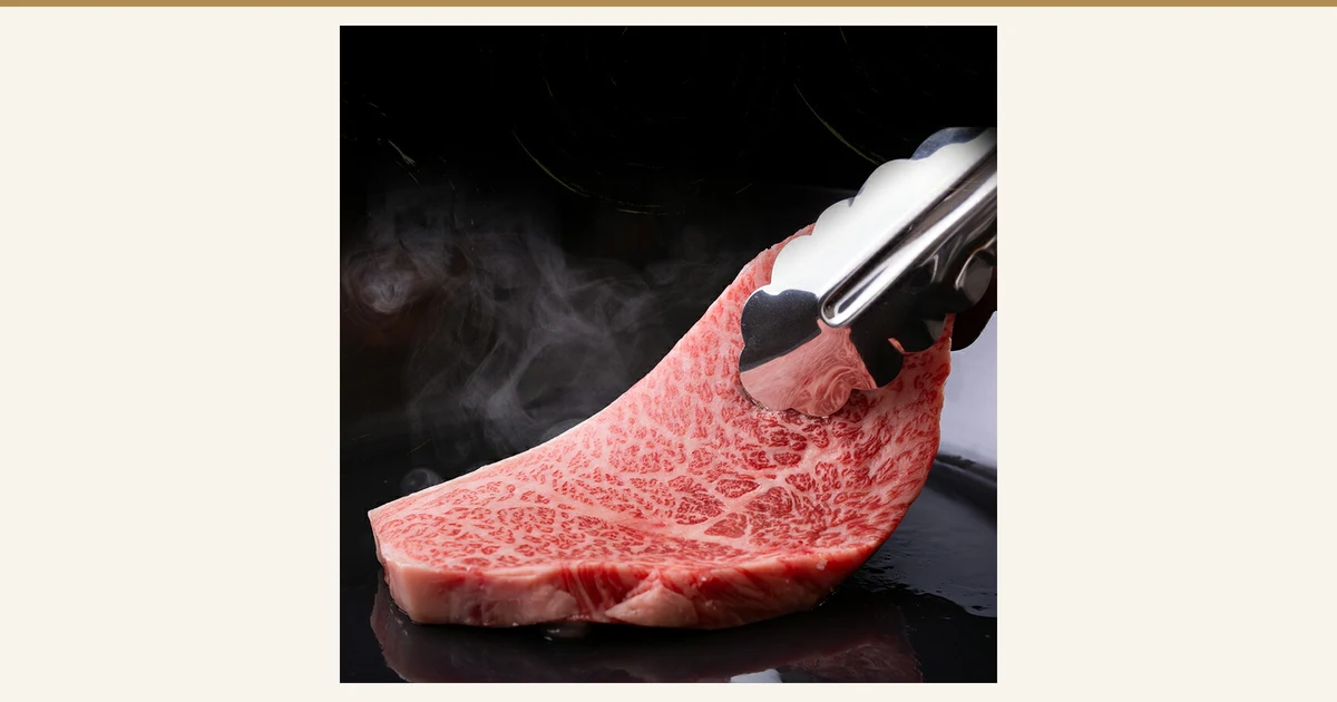 A5黑毛和牛 サーロイン（西冷）600g（良肉問屋）的封面图。黑色铁板上热气升腾，用夹子夹起一块雪花纹理的西冷牛排的照片。图片中没有文字。