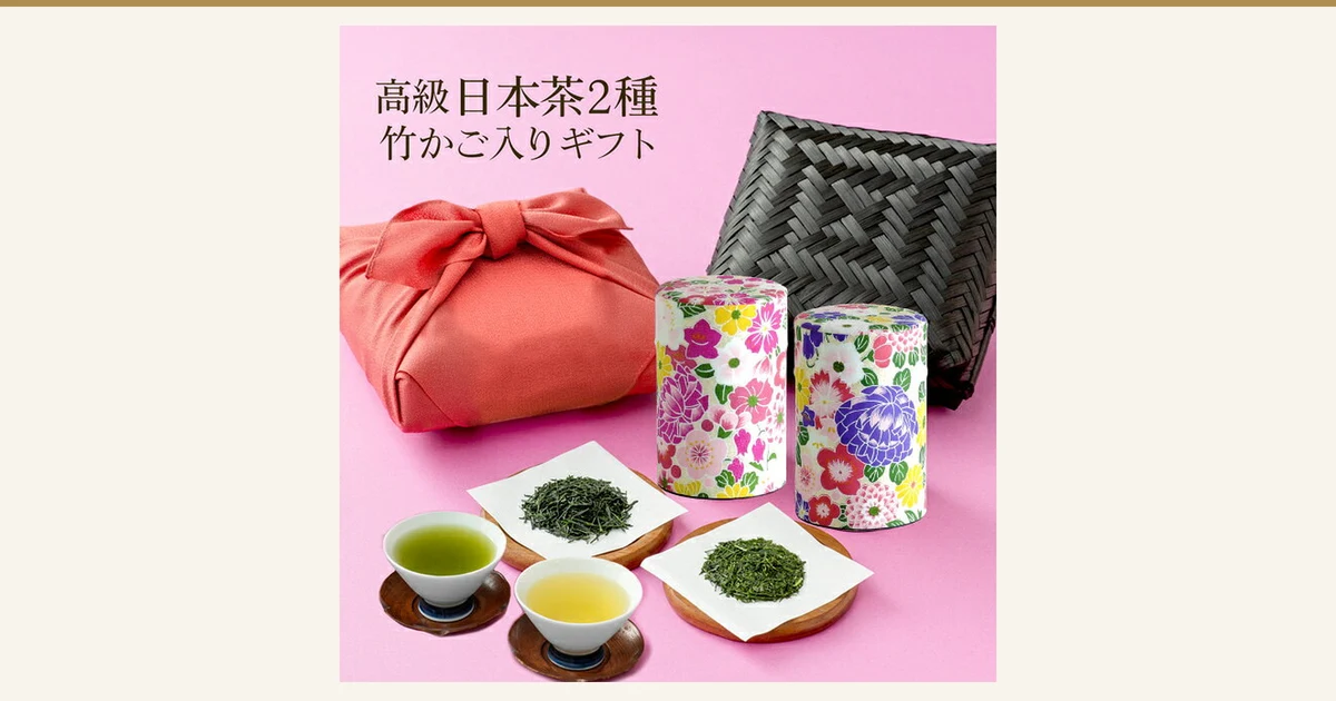 ピンク色の背景に、ローズ色の風呂敷包み・黒い竹かご・花柄の茶缶2つ・茶葉をのせた紙・淹れたお茶の茶碗2つを並べた商品写真（川本屋茶舗 秋の蔵出し新茶と掛川茶の竹籠セット）。店舗が画像に入れた表示「高級日本茶2種 竹かご入りギフト」。淹れたお茶・茶碗・茶托・茶葉をのせた紙と台は商品に含まれません