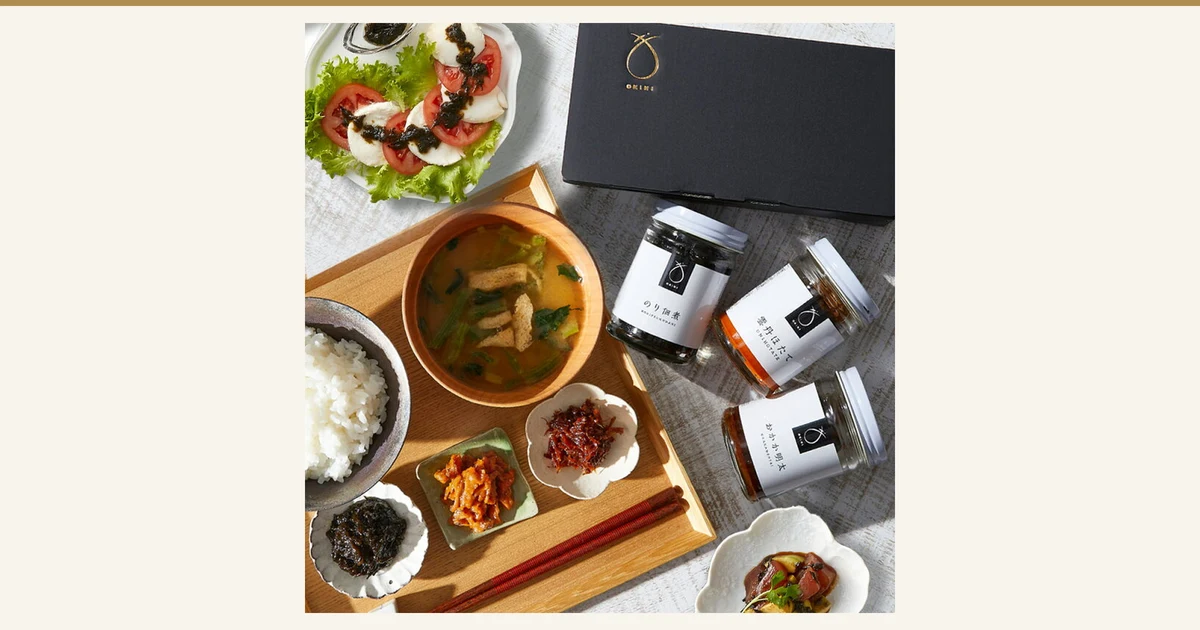 OKiNI 佃煮瓶3本セット 小倉屋山本のアイキャッチ。黒い専用化粧箱と、のり佃煮・雲丹ほたて・おかか明太の瓶3本を、ご飯・味噌汁・小皿の佃煮・トマトとチーズのサラダとともに上から撮った写真。ご飯・味噌汁・サラダ・器は盛り付けの例で、商品に含まれない。画像内の文字は瓶のラベル(「のり佃煮」「雲丹ほたて」「おかか明太」「OKINI」)のみ。