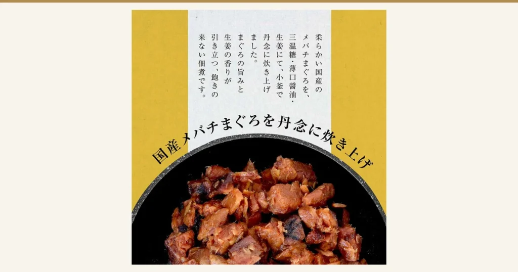 Close-up photo of maguro kakuni served in a black dish (大熊 Maguro Kakuni Mini Size Teiban 3 Bags). Text the shop added to the image: “柔らかい国産のメバチまぐろを、三温糖・薄口醤油・生姜にて、小釜で丹念に炊き上げました。まぐろの旨みと生姜の香りが引き立つ、飽きの来ない佃煮です。” (Tender domestic bigeye tuna simmered carefully in a small kettle with brown sugar, light soy sauce and ginger. A tsukudani you will not tire of, with the umami of tuna and aroma of ginger) and “国産メバチまぐろを丹念に炊き上げ” (Domestic bigeye tuna simmered with care)