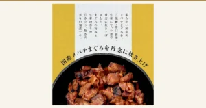 盛在黑色器皿中的まぐろ角煮（金枪鱼角煮）特写照片（大熊 まぐろ角煮 ミニサイズ 定番3袋）。店铺加入图片中的文字「柔らかい国産のメバチまぐろを、三温糖・薄口醤油・生姜にて、小釜で丹念に炊き上げました。まぐろの旨みと生姜の香りが引き立つ、飽きの来ない佃煮です。」（用小锅仔细炖煮柔软的国产大眼金枪鱼，加入三温糖、淡口酱油和生姜。突出金枪鱼的鲜味与生姜的香气，百吃不腻的佃煮）以及「国産メバチまぐろを丹念に炊き上げ」（仔细炖煮国产大眼金枪鱼）