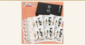 黒い化粧箱「琴線」の手前に、半生うどん6袋とつゆの小袋6つを並べた商品ページの写真（こんぴらや）。店舗ロゴ入り。化粧箱は品切れの際、白い箱に変更になる注意書きが商品ページにあります