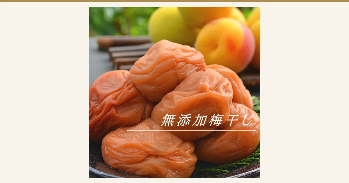 Photo of wrinkled, glossy orange-pink umeboshi piled together with ripe yellow-and-blush ume fruit behind them (Mutenka Umeboshi 600g, 古道の梅屋). Text the shop added to the image: “無添加梅干し”
