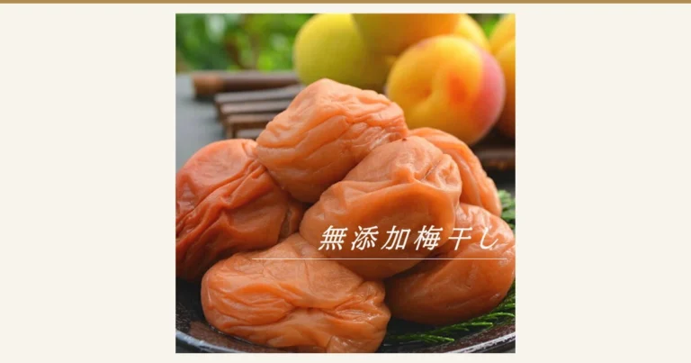 つやのある橙がかったピンク色でしわのある梅干しが積み重なり、背後に黄色く赤みのさした梅の実が写る商品写真（無添加梅干し 600g 古道の梅屋）。店舗が画像に入れた表示：「無添加梅干し」