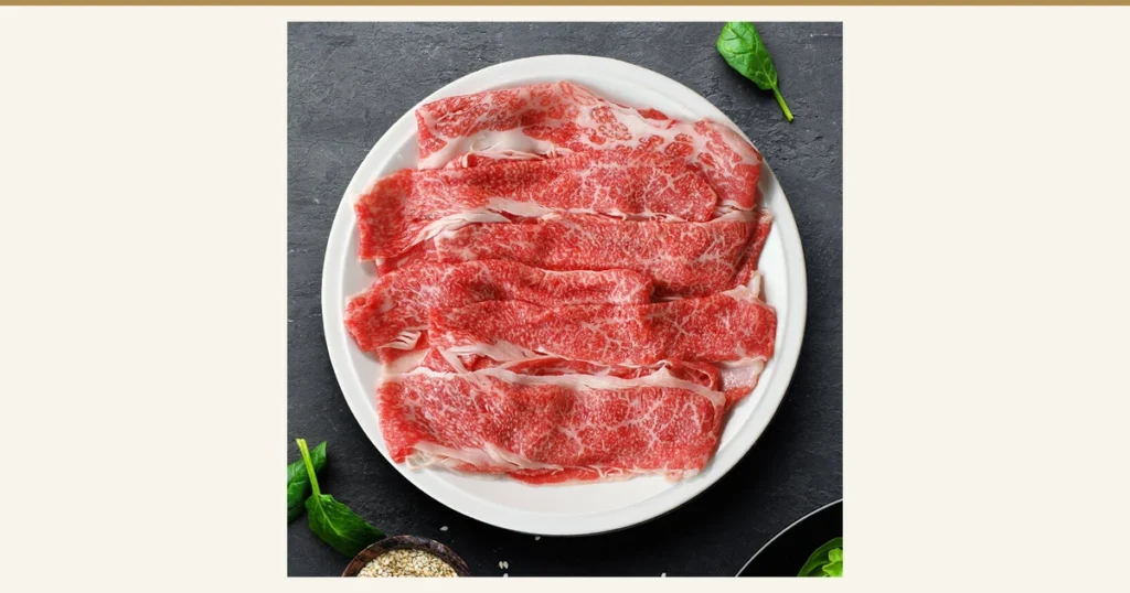 Product photo of Meat Tamaya Kuroge Wagyu off-cuts for sukiyaki, 1.2kg: thinly sliced beef laid out on a white round plate. Spinach leaves and sesame seeds appear beside the plate as props and are not included in the product.