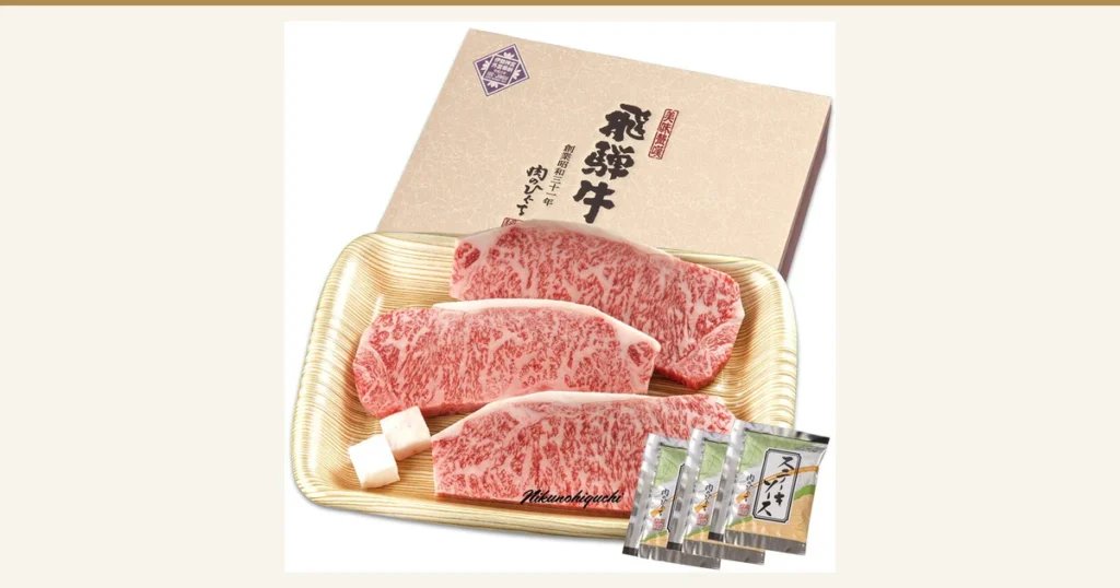 飛騨牛 サーロインステーキ 計500g（165g位×3枚）の記事アイキャッチ。飛騨牛 サーロインステーキ 計500g（165g位×3枚）の商品写真。木目調のトレイに生のサーロインステーキ3枚と付属のステーキソース3袋がのり、後ろに化粧箱が立てかけられている。画像内の文字は店舗が入れた表示で、箱に「美味歓饌」「飛騨牛」「創業昭和三十一年 肉のひぐち」の文字と小さな奉納のマーク、写真の下部に「Nikunohiguchi」の署名風の文字がある。