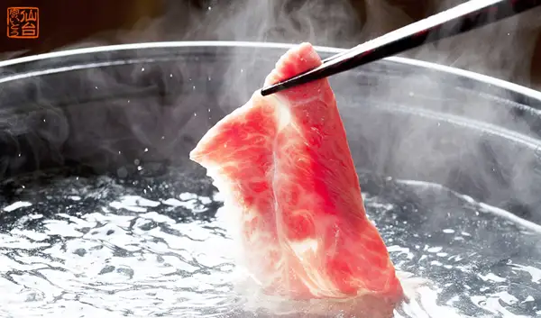 用筷子夹起薄切牛肉、放入冒着热气的锅中热水里涮煮的涮涮锅烹调示例照片。这是能看出收到后吃法的、上質 仙台黒毛和牛 特選 すき焼き・しゃぶしゃぶ用 ロース 400g的店铺发布照片。图片中店铺自行加入的标示：左上角有「仙台 肉のいとう」的标志。