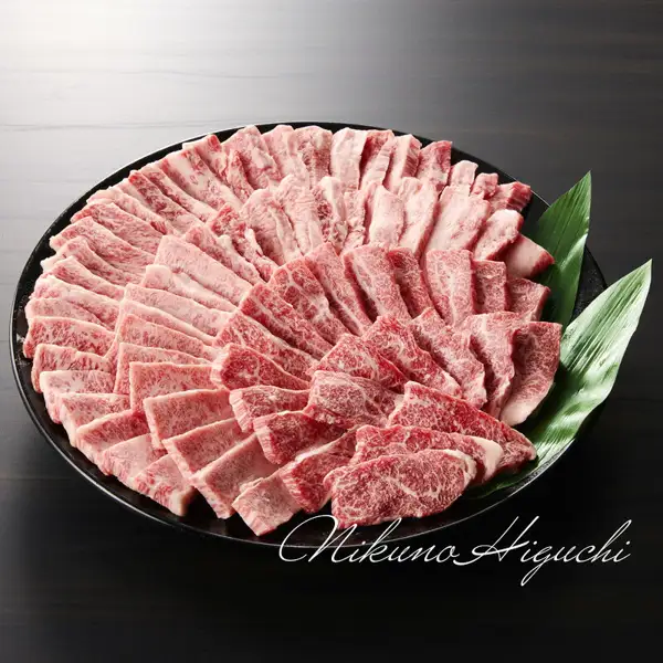飛騨牛カルビ 焼肉用 メガ盛り1kg的商品照片:黑色圆盘中呈放射状摆放着带有红肉和白色脂肪的烤肉用薄切牛肉,并配有竹叶。照片下部有店铺名的草书体水印。