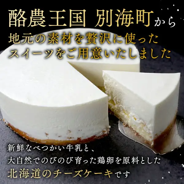 Product photo of a round white cheesecake with one cut slice taken out, set side by side on a dark stone-like stand (Rich Cheesecake BETSUKAI, a furusato nozei thank-you gift from Betsukai Town, Hokkaido). Text the shop placed in the image reads “酪農王国 別海町から 地元の素材を贅沢に使ったスイーツをご用意いたしました” (From Betsukai, the dairy kingdom: sweets made lavishly with local ingredients) and “新鮮なべつかい牛乳と、大自然でのびのび育った鶏卵を原料とした北海道のチーズケーキです” (A Hokkaido cheesecake made from fresh Betsukai milk and eggs from hens raised freely in nature)