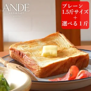Product photo of a slice of Danish bread toasted with a pat of butter on top, on a white plate, with ham at the edge of the plate and lettuce in a wooden bowl in front (ANDE Danish Bread, plain 1.5-kin loaf + 1-kin loaf of your choice). Text the shop placed in the image: “ANDE BREAKFAST KYOTO”, “プレーン1.5斤サイズ+選べる1斤” (plain 1.5-kin size + 1-kin loaf of your choice)