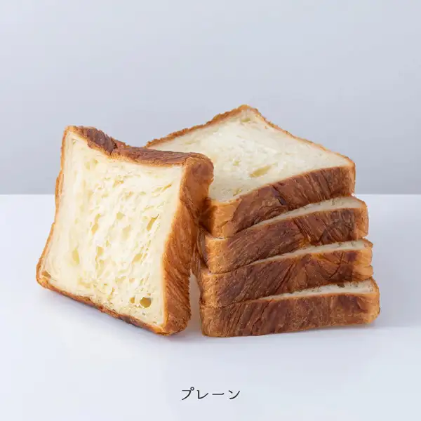京都祇園ボロニヤ 元祖デニッシュ食パン 1斤スライス3個の商品写真。白い台の上に、5枚にスライスされたプレーンのデニッシュ食パンが置かれている。1枚は手前に立てかけられ、残りの4枚は奥に重ねてある。断面は白っぽく、耳は濃い焼き色。店舗が画像に入れた表示「プレーン」