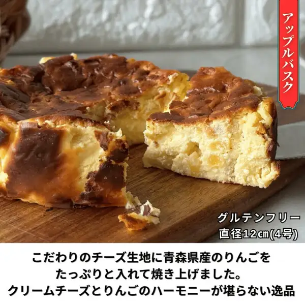 iBASQUE バスクチーズケーキ 4号のアップルバスクを木のまな板の上で切り分けた商品写真。断面にりんごの角切りが見える。店舗が画像に入れた表示「アップルバスク」「グルテンフリー 直径12㎝(4号)」「こだわりのチーズ生地に青森県産のりんごをたっぷりと入れて焼き上げました。クリームチーズとりんごのハーモニーが堪らない逸品」