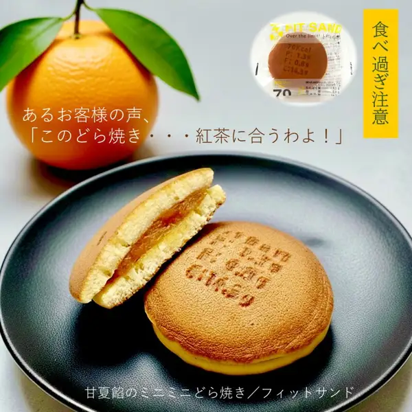 灰色背景中的黑色圆盘上,并排放着切开后可见黄色馅料的铜锣烧和表面有烙印文字的铜锣烧,后方是带叶子的甘夏蜜柑果实的照片。左上方写着某位顾客的评价,大意是这款铜锣烧很配红茶;右上方黄色横条上写着「食べ過ぎ注意」,其下的圆圈中有一张独立包装小袋的照片,下方写着「甘夏餡のミニミニどら焼き/フィットサンド」(店舗在图片中加入的标示)。 菓匠 津具屋本舗 ミニどら焼き(迷你铜锣烧)14个装 独立包装