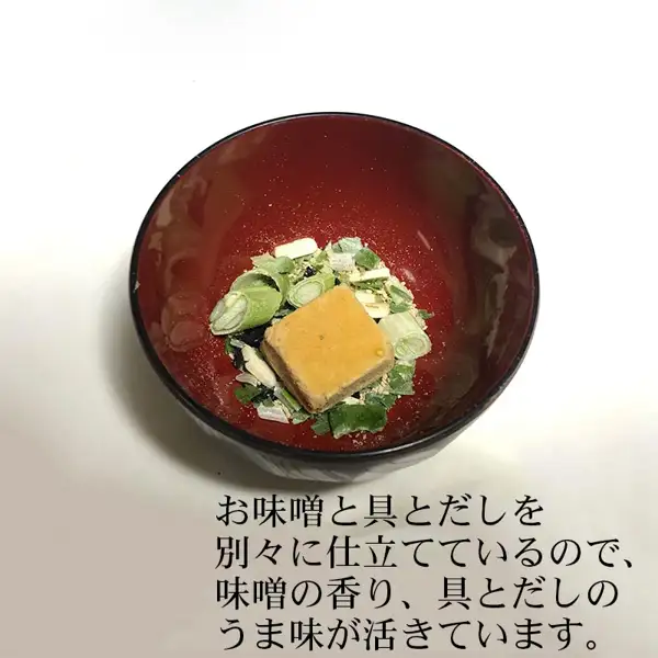しま村のフリーズドライ だし香る味噌汁 10食の商品写真。赤い椀に入った、お湯を注ぐ前のフリーズドライの味噌のかたまりと、ねぎなどの具。店舗が画像に入れた表示「お味噌と具とだしを別々に仕立てているので、味噌の香り、具とだしのうま味が活きています。」