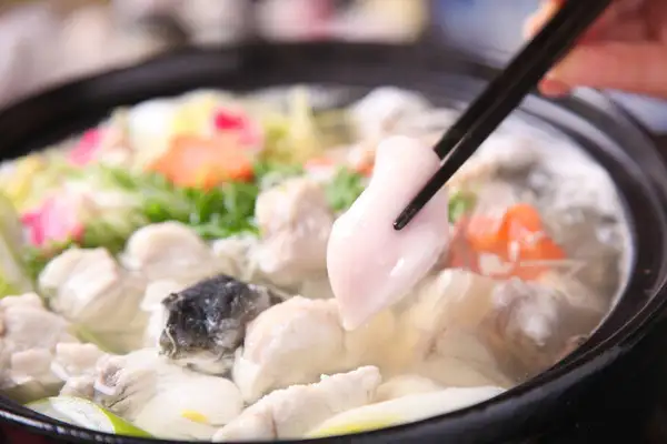土鍋でとらふぐの身やアラ、野菜などを煮た鍋の調理例の写真。箸でとらふぐの身をつまみ上げている（野菜などの具材は商品に含まれない）。店舗の商品ページに載る、淡路島3年とらふぐ 若男水産 丸ごと1匹身欠きの食べ方の一例