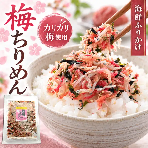 梅ちりめん カリカリ梅入りソフトふりかけ（うめ海鮮）の盛り付け例の写真。白っぽい器に盛った白いご飯に、ちりめん・赤いカリカリ梅・ひじき・わかめ・ごまが混ざったふりかけをたっぷりのせ、箸でつまみ上げている。左下にピンクのラベルの付いた透明な袋入りの商品1袋、背景にぼかした赤い食材を盛った器と緑の葉、桜の花の飾りが写る（ご飯と背景の器の食材は商品に含まれません）。画像内に店舗が画像に入れた表示として「梅ちりめん」「カリカリ梅使用」「海鮮ふりかけ」の文字、袋のラベルに「自然の恵み 海の幸」「梅」「ちりめん」の文字あり。